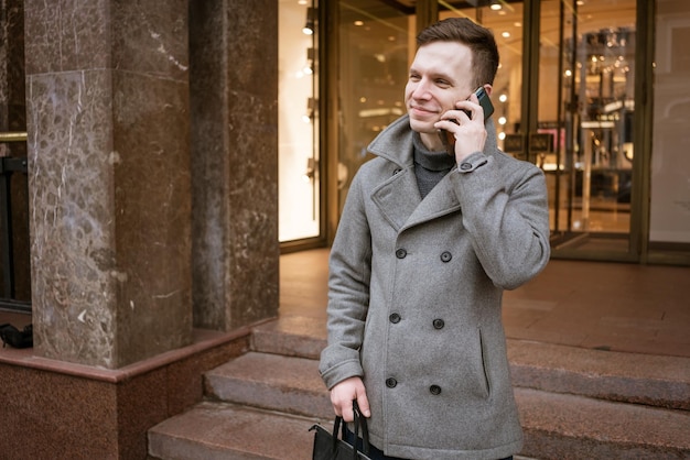 Man in gray coat and sweater stands on city street Talks on phone Solves