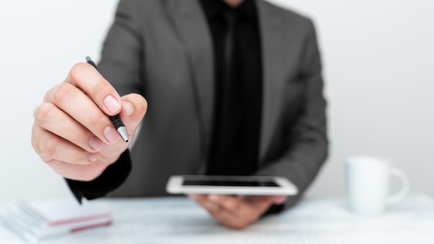 Man in Gray jacket sitting at white table And Pointing With Pen On Important Message Holding mobile phone Gentleman Showing Critical Announcement