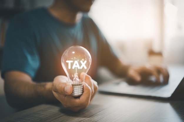 Man hand holding light bulb while working on laptop and mobile phone With tax messages conveys tax deductions at the end of the year paying taxes Finance tax business investment concept