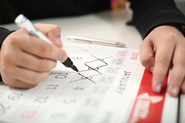 Man hand holding a pen and draws a cross on calendar Calendar icon