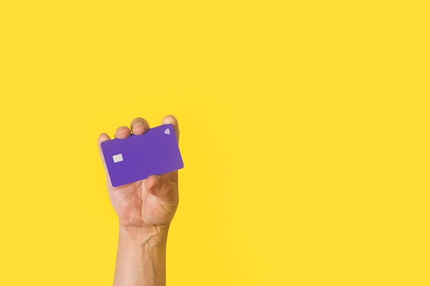 Man hand holding a purple credit card on a yellow background