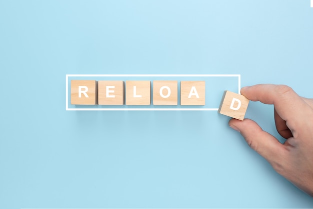 Man hand holding wooden cube with reload word on blue background.