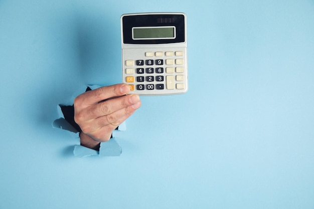 A man hand holds a calculator on blue background