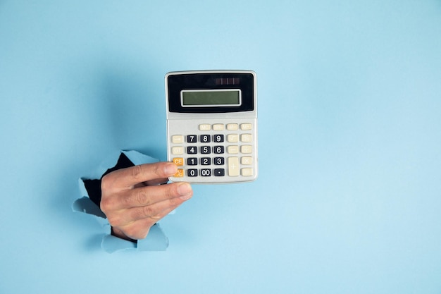 A man hand holds a calculator on blue background