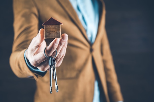 Man hand house model with key on dark background