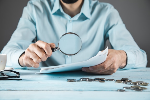 Man hand magnifier and document with coins on the table