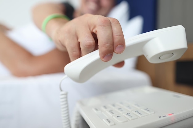 Man hand picking up receiver of phone in bedroom closeup hotel room service concept