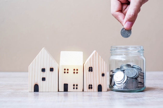 Man hand putting coin in glass jar and wooden house model