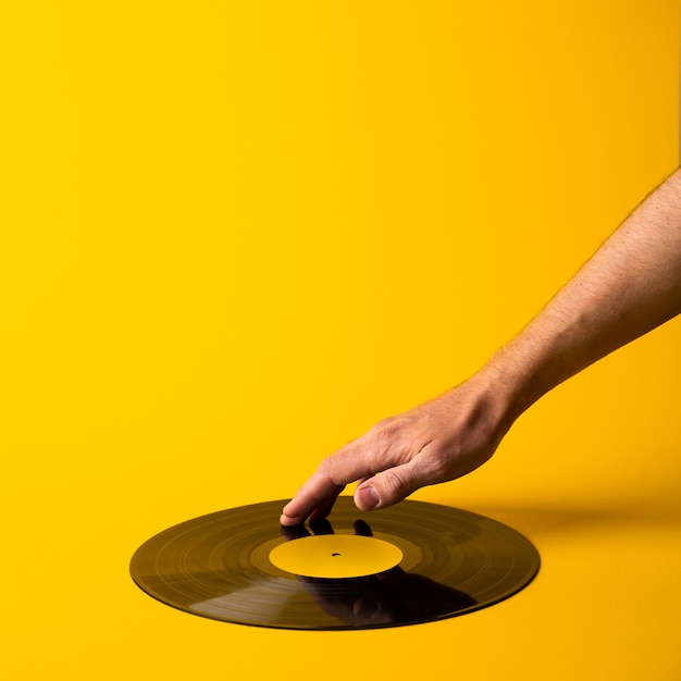 Man hand touches vinyl record on abstract yellow background