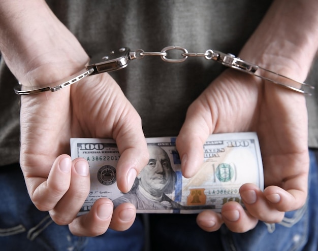 Man in handcuffs holding dollar banknotes behind the back close up