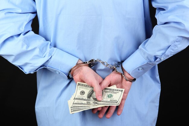 Man in handcuffs is holding dollars on black background