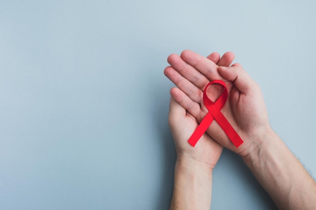 Man hands hold red ribbon awareness Aids on light blue background