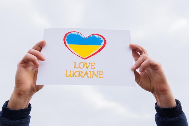 Man hands holding of heart drawingon the cardboard with words love ukraine protesting against the ru