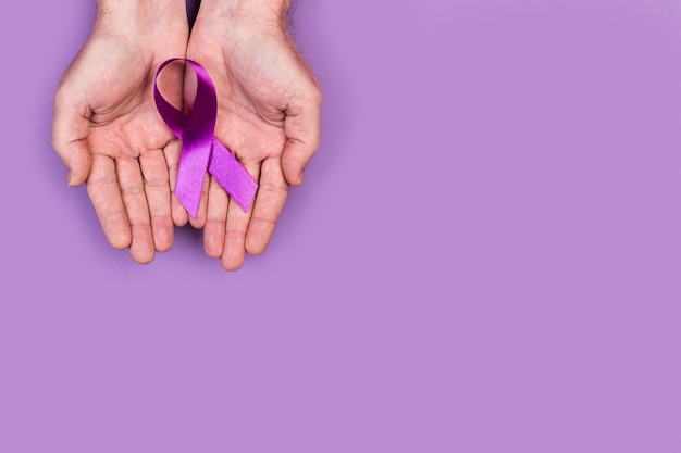 Man hands holding a purple ribbon on a purple background with copy space