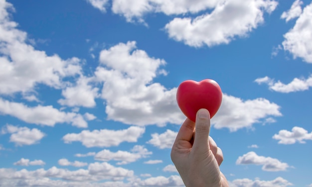 man hands holding red heart up to blue sky