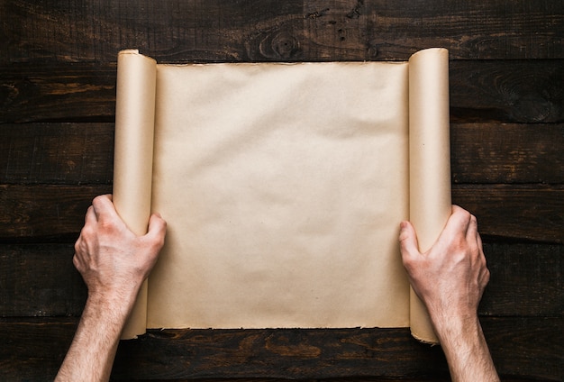 Man hands holding stressed paper roll on old barwood background. Wanderlust expedition creative concept. Empty space, room for text, lettering. Horizontal banner mockup.