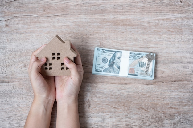 Man hands holding Wood house model beside money of American dollar 