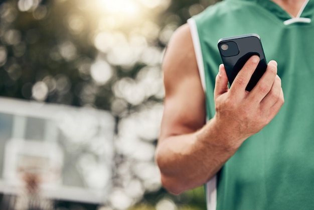 Man hands and phone in sports communication and social media for basketball in the nature outdoors Muscular male in sport fitness exercise and game time check message or text on mobile smartphone