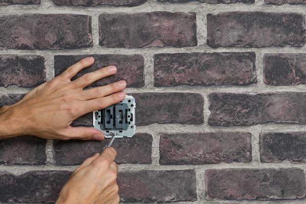 Man hands with screwdriver disassembling a switch installed in a fake brick wall