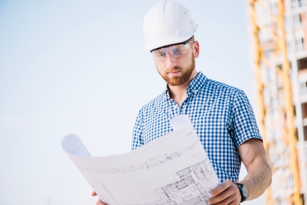 Man in hardhat looking at blueprint paper