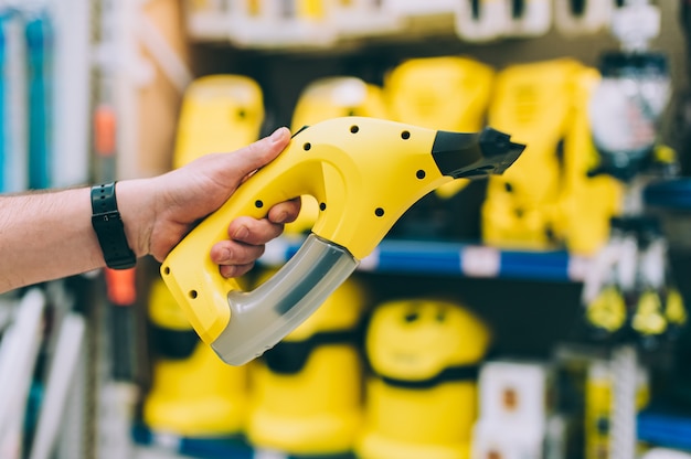 A man in a hardware store holds a garment steamer.