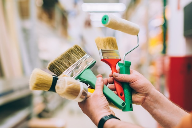 A man in a hardware store holds a set of brushes and rollers for paint and decor.