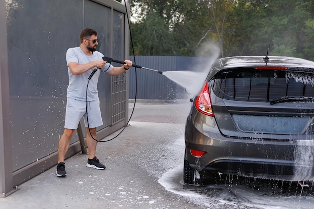 The man has a water cannon in his hand that she uses to wash the car A car at a self service car wash