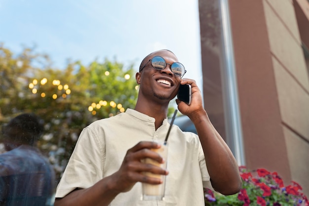 Man having an iced coffee break while using smartphone outdoors