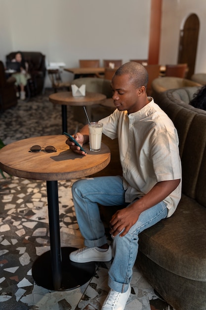 Man having an iced coffee break while using smartphone