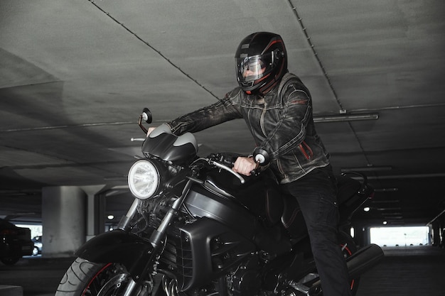 A man in a helmet sitting on a motorcycle in underground parking garage