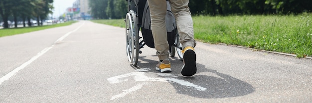 Man helping disabled person in wheelchair to walk on sidewalk