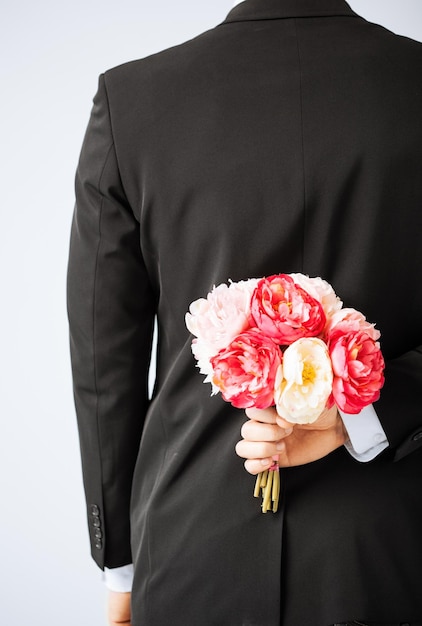 man hiding bouquet of flowers behind his back.