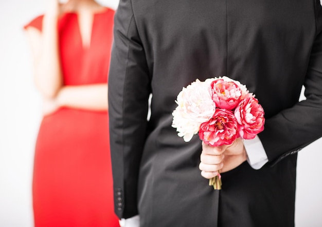 man hiding bouquet of flowers behind his back.