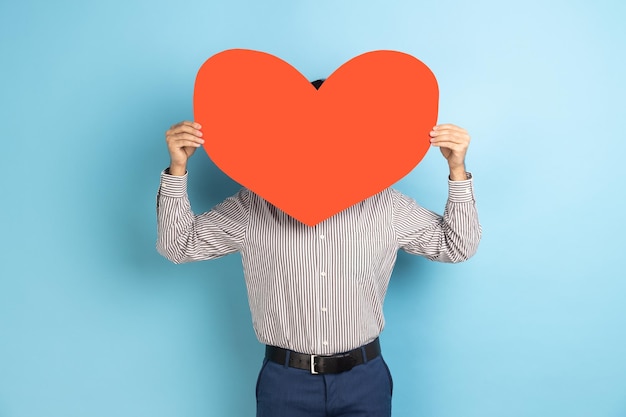 Man hiding his face behind big read paper heart holding symbol of love care generosity give hope