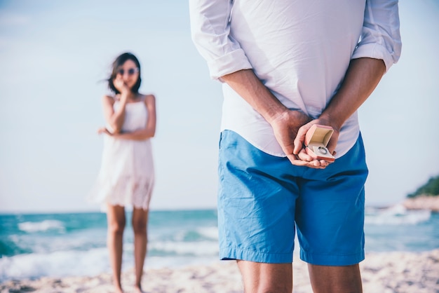 Man hiding a ring behind for making surprise proposal to his girlfriend at the beach.