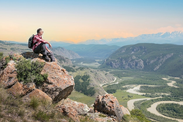 Man hiker sitting on cliff and enjoying valley view at sunset