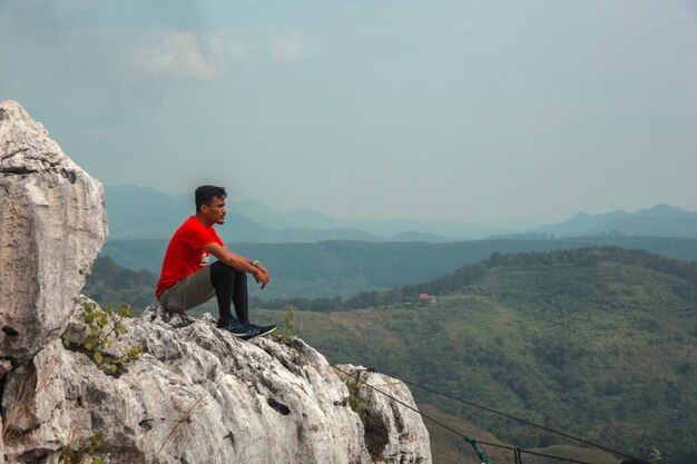 Photo man hiker sitting on top hill and enjoying amazing view on bright blue sky