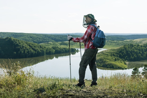 Man hiker with nets from mosquitoes in hiking trip near lake outdoors.