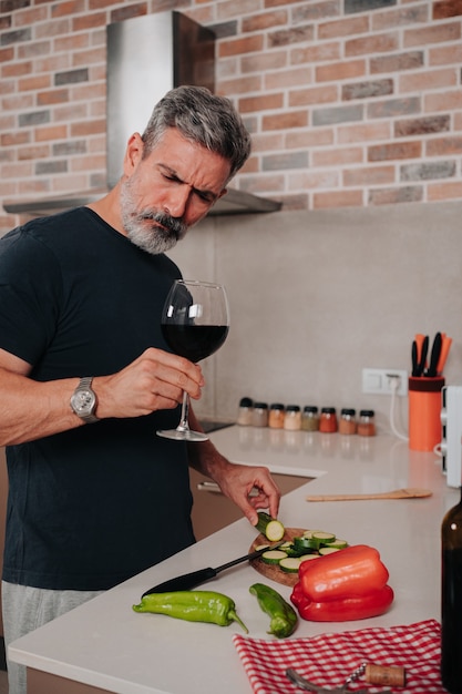 Man in his 50s making food while having a glass of wine