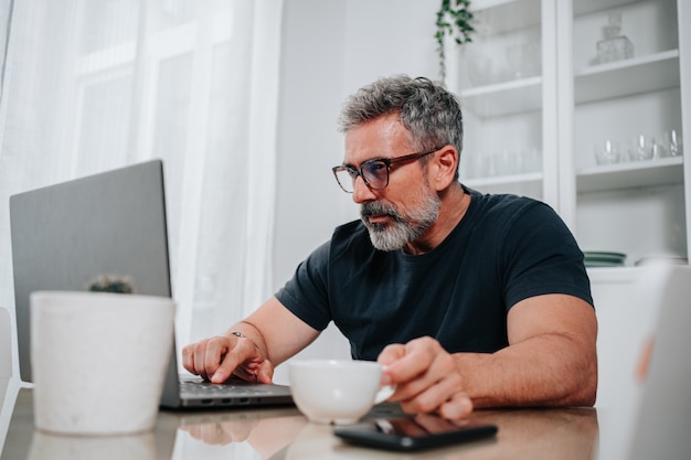 Man in his 50s working from home while having a coffee and is on video call on the computer