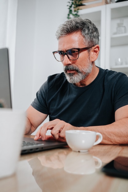 Man in his 50s working from home while having a coffee and is on video call on the computer