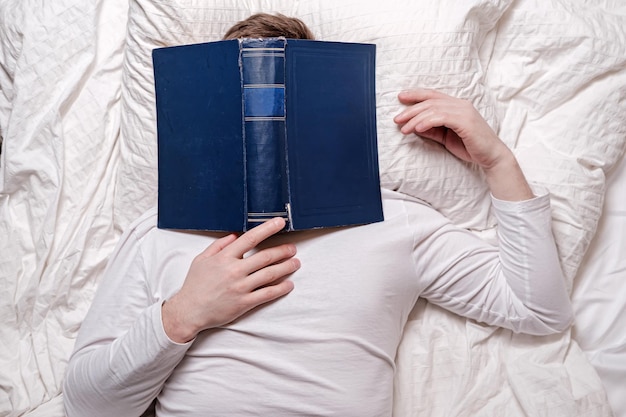 Man in his pajamas fell asleep reading and the book covered his face