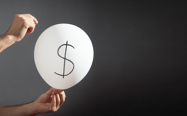 Man hold needle directed to balloon Dollar symbol on balloon