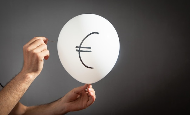 Man hold needle directed to balloon Euro symbol on balloon