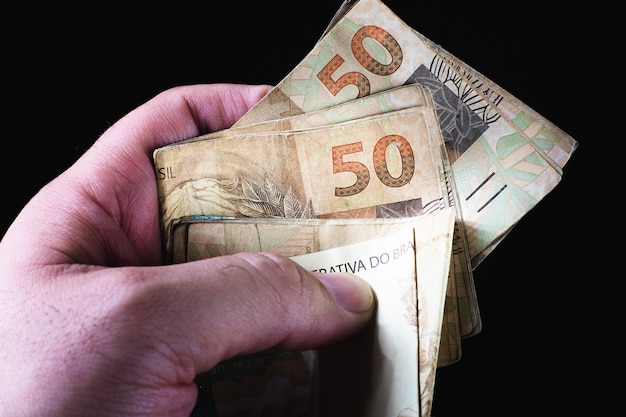 a man holding a 100 bill of brazil money which is the brazilian real on black background