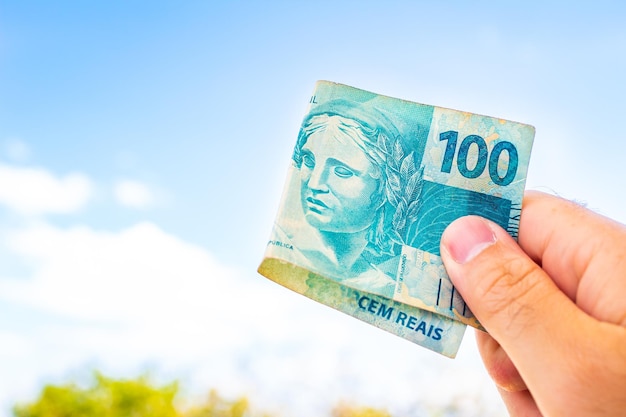 A man holding a 100 Brazilian Real bill