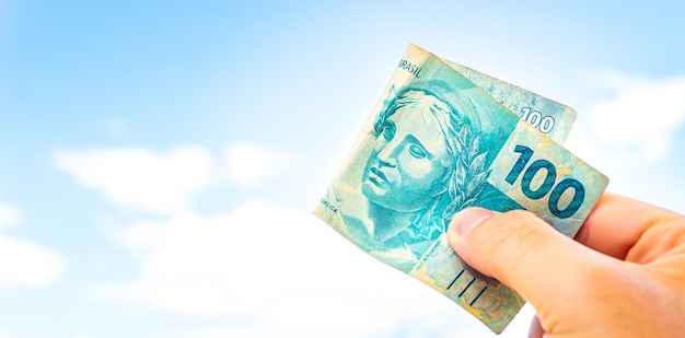 A man holding a 100 Brazilian Real bill