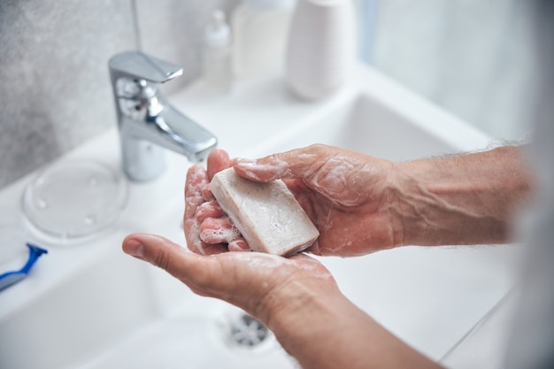  man holding a bar of natural soap on his palms over the sink