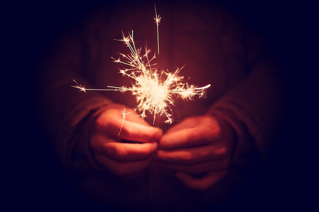 Man holding bright festive Christmas sparkler in hand, tinted photo