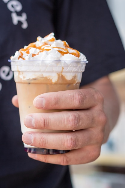 Man holding cold latte with whipped cream Iced latte decorated with salt caramel topping in hand